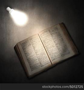 Book and light bulb. Old opened book and glowing light bulb