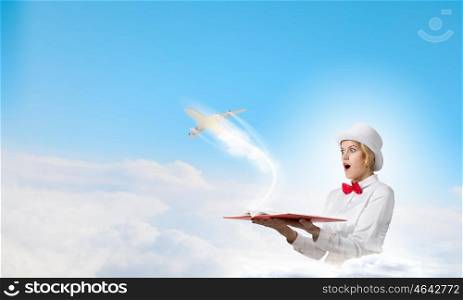 Book that blow up your imagination. Young woman in white hat with opened book in hands and airplane flying out