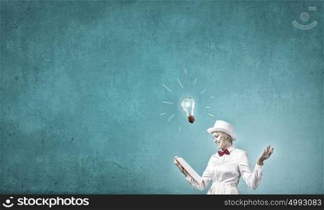 Book that blow up your imagination. Young woman in white hat with opened book in hands and glass light bulb on pages
