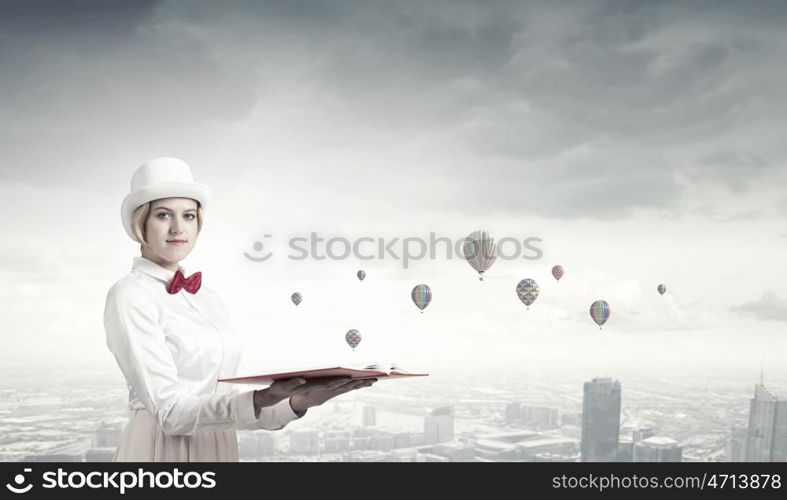 Book that develope your imagination. Young woman in white cylinder and red bowtie with book in hands