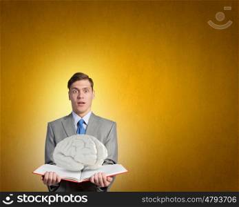 Book to broaden your mind. Shocked businessman holding opened book with brain picture