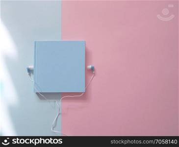 Book with earphones on a bue and pink background. Audio books concept