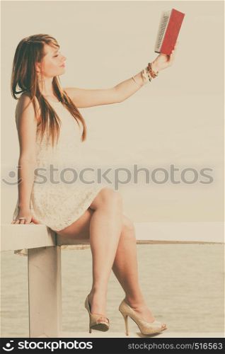 Books, bookworm, travel, leisure time concept. Beautiful woman wearing white dress sitting on wooden hurdle near sea and book in the air. Woman sitting on hurdle near sea, reading book
