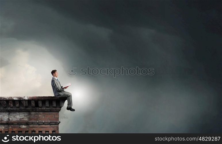 Books broaden your mind. Young businessman sitting on building top and reading book