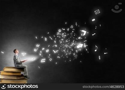 Books broden your mind. Young businessman sitting on pile with book in hands