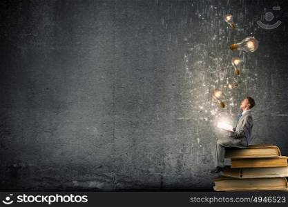 Books broden your mind. Young businessman sitting on pile with book in hands
