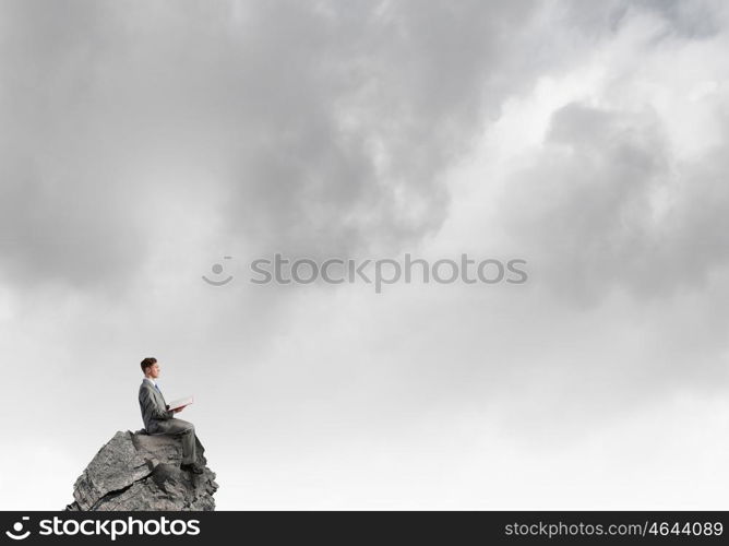 Books broden your mind. Young businessman sitting on rock top with book in hands