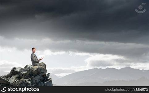 Books broden your mind. Young businessman sitting on rock top with book in hands