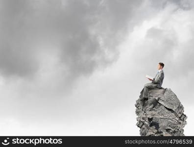 Books broden your mind. Young businessman sitting on rock top with book in hands