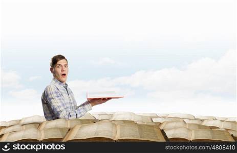 Books let you rise above the rest. Young handsome man in pile reaching hand with book
