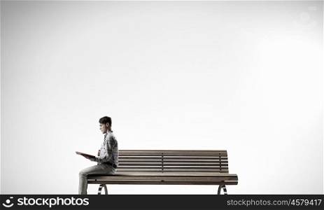 Books let you rise above the rest. Young man in casual sitting on wooden bench with book in hands