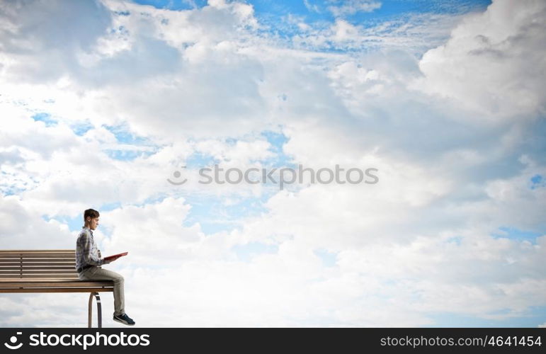 Books let you rise above the rest. Young man in casual sitting on wooden bench with book in hands