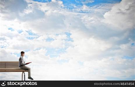 Books let you rise above the rest. Young man in casual sitting on wooden bench with book in hands