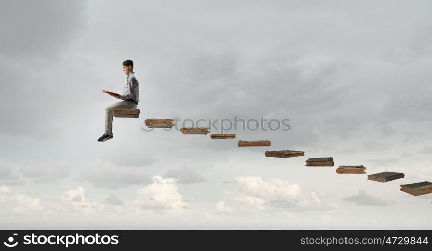 Books let you rise above the rest. Young man in casual sitting on stair steps with book in hands