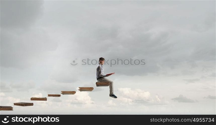 Books let you rise above the rest. Young man in casual sitting on stair steps with book in hands
