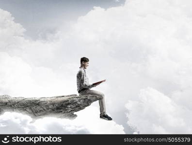 Books let you rise above the rest. Young man in casual sitting on rock top with book in hands