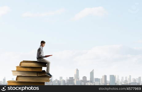 Books let you rise above the rest. Young man sitting on pile of old books with one in hands