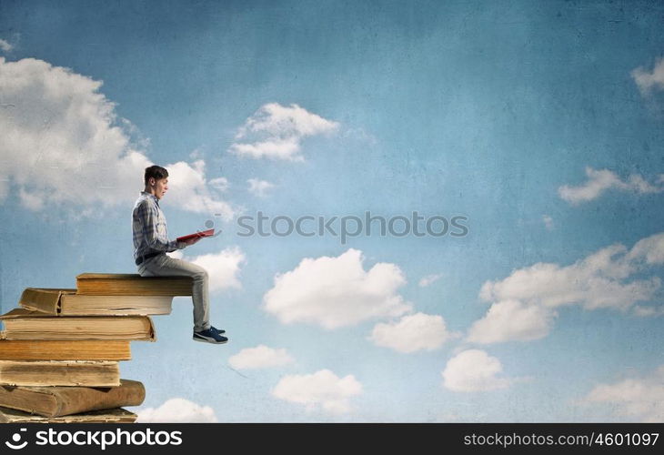 Books let you rise above the rest. Young man sitting on pile of old books with one in hands