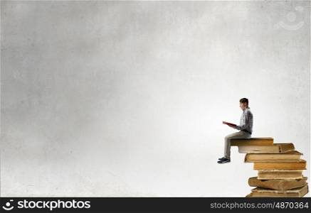 Books let you rise above the rest. Young man sitting on pile of old books with one in hands