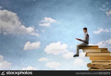 Books let you rise above the rest. Young man sitting on pile of old books with one in hands