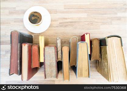 Books row on wooden table with cup of coffee, top view flat lay. Reading, learning, literature concept. Pile of old books