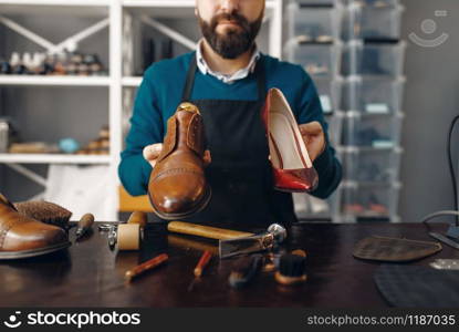 Bootmaker shows repaired shoes, footwear repair service. Craftsman skill, shoemaking workshop, master works with boots, cobbler. Bootmaker shows repaired shoes, footwear repair