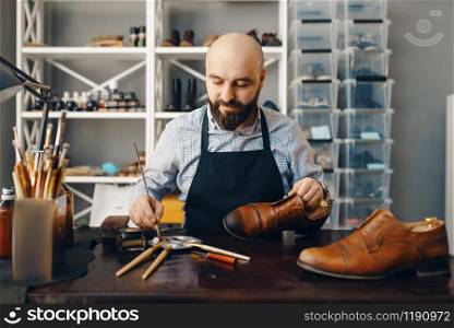 Bootmaker with brush tints shoes, footwear repair service. Craftsman skill, shoemaking workshop, master works with boots. Bootmaker with brush tints shoes, footwear repair