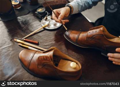 Bootmaker with brush tints shoes, footwear repair service. Craftsman skill, shoemaking workshop, cobbler shop. Bootmaker with brush tints shoes, footwear repair