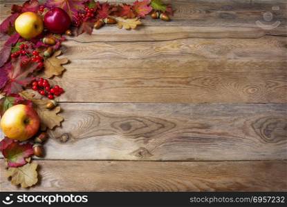 Border of apples, acorns, berries and fall leaves on the old woo. Border of apples, acorns, berries and fall leaves on the old wooden background. Thanksgiving background with seasonal berries and fruits. Abundant harvest concept.