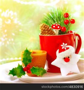 Border of Christmastime utensil set, red tea cup standing on white plate and decorated with Santa Clause star toy, yellow candle, twig of berry, fir cone and branch of Christmas tree, holiday dinner