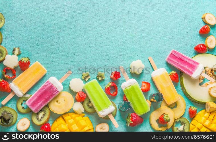 Border of Colorful various Ice cream popsicles with fresh sliced fruits and berries ingredients on light blue background, top view, flat lay. Frozen tropical juices. Homemade ice cream