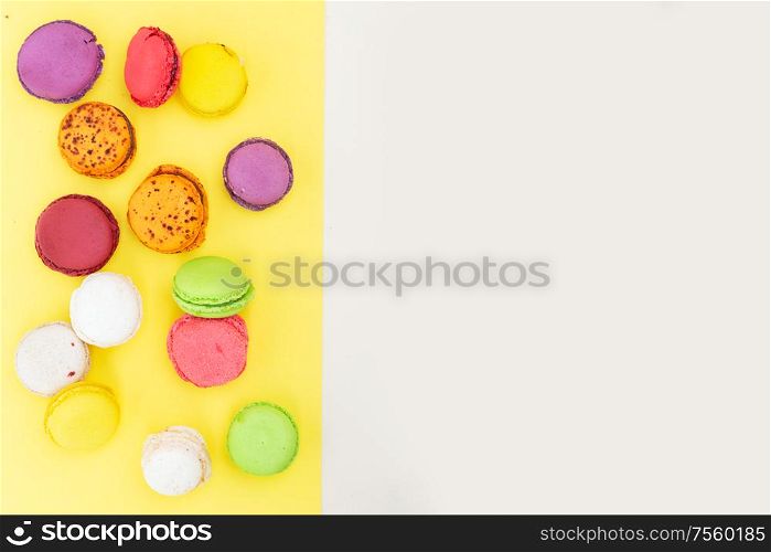 Border of fresh fresh macaroon biscuit, top view over yellow and beige background. Fresh macaroon confection