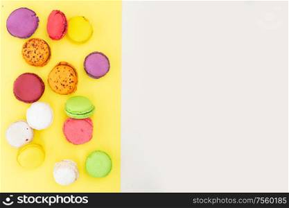 Border of fresh fresh macaroon biscuit, top view over yellow and beige background. Fresh macaroon confection