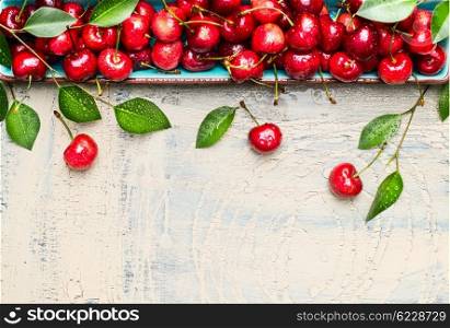 Border of sweet cherries with green leaves on light wooden background, top view, place for text. Summer fruits and berries concept.