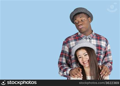Bored African American man with smiling girlfriend over blue background