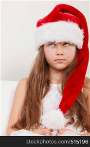 Bored cute little girl kid in red santa claus hat and white dress. Chrtistmas holiday season.. Bored little girl kid in santa hat. Christmas.