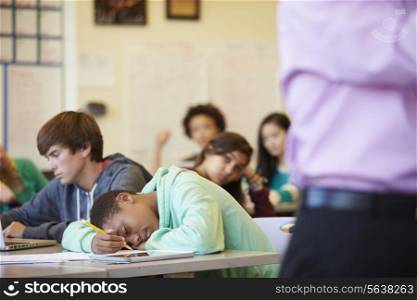 Bored High School Pupil Slumped On Desk In Classroom