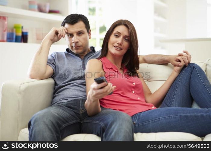 Bored Husband Sitting With Wife On Sofa Watching TV