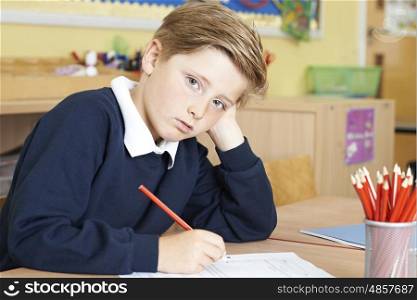 Bored Male Elementary School Pupil At Desk