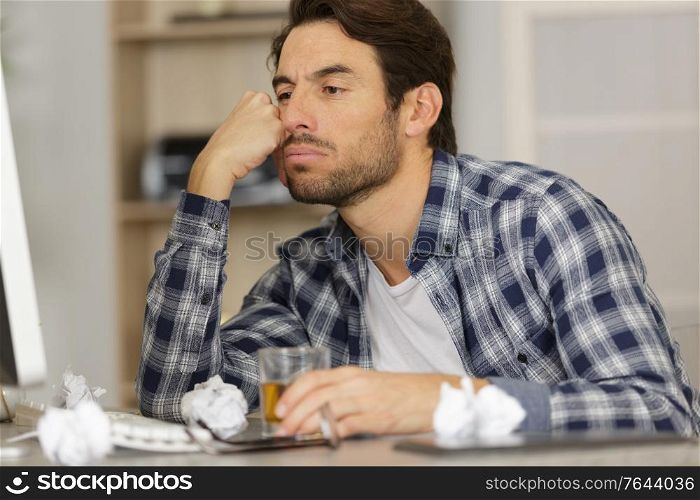 bored man with drink sat in front of his computer