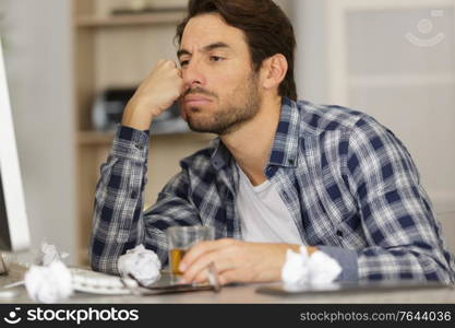 bored man with drink sat in front of his computer