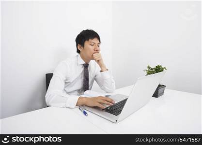 Bored mid adult businessman using laptop at desk in office