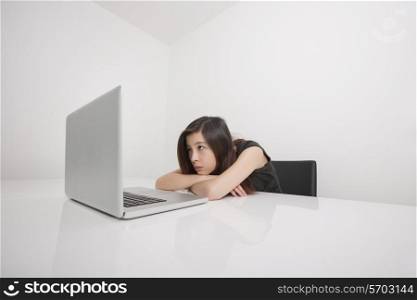 Bored young businesswoman looking at laptop in office