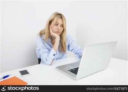 Bored young businesswoman using laptop at desk in office
