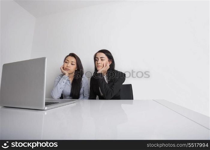 Bored young businesswomen using laptop at desk in office