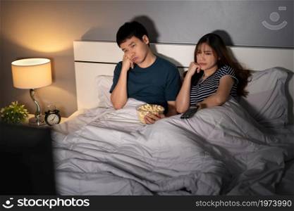 bored young couple watching TV on a bed at night