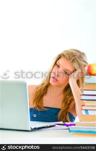 Bored young girl sitting at table and looking on laptop&#xA;