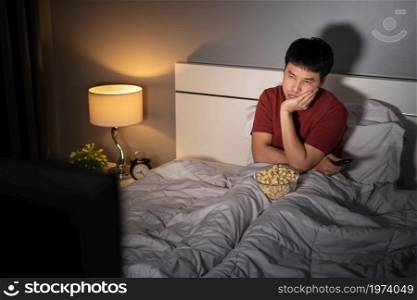 bored young man watching TV on a bed at night
