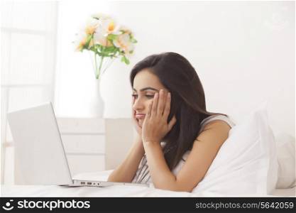 Bored young woman looking at laptop in bed