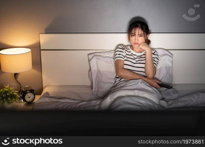 bored young woman watching TV on a bed at night